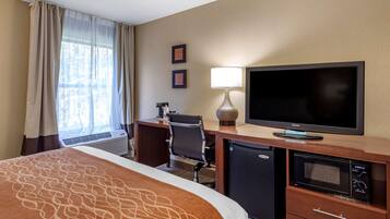 Habitación de hotel con cama, escritorio con computadora, televisión, microondas y refrigerador pequeño.