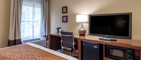 Habitación de hotel con cama, escritorio con computadora, televisión, microondas y refrigerador pequeño.
