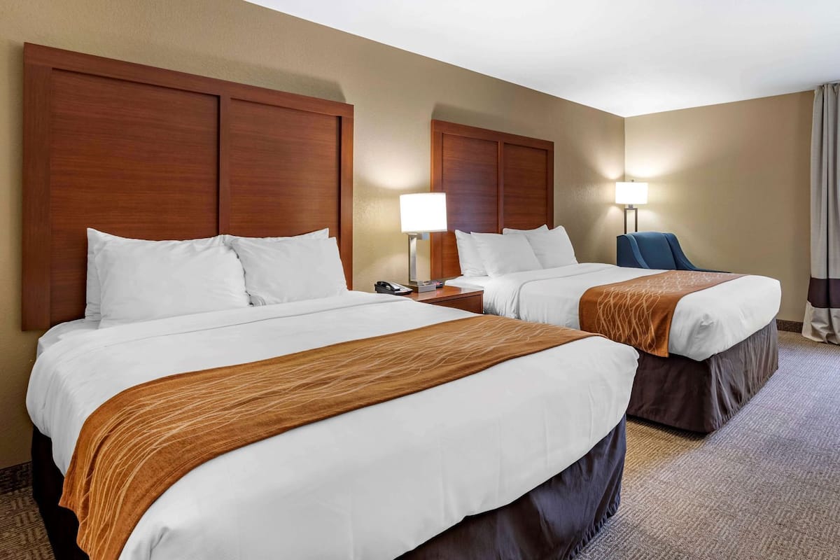 Ein Hotelzimmer mit zwei Betten, Holz-Kopfteilen, weißer Bettwäsche, einer braunen Decke und einer Lampe.