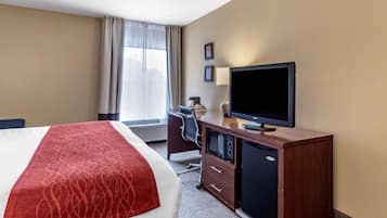 A hotel room with a bed, a desk with a computer, a television, and a window with curtains.