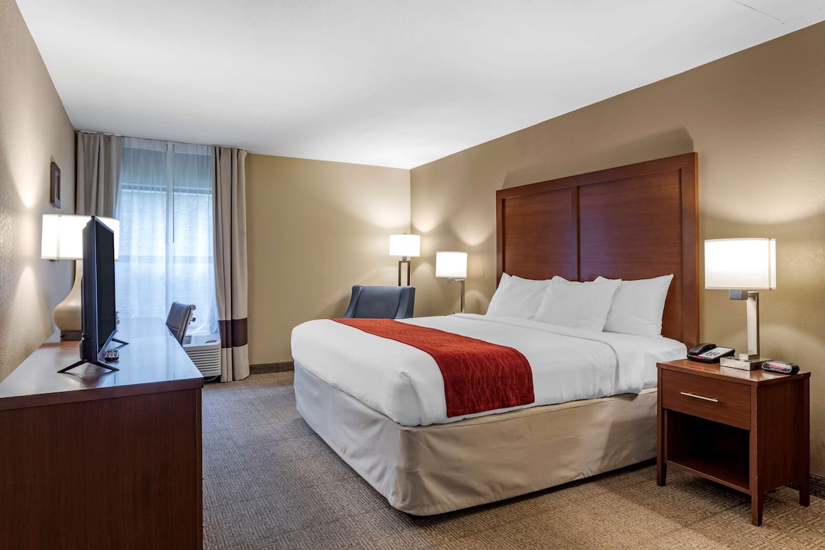 A hotel room with a bed, bedside tables, a desk with a computer, and a TV.