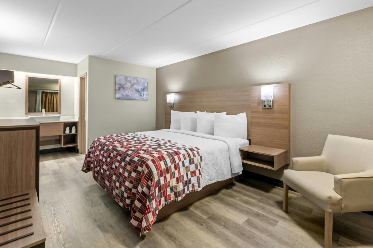 A hotel room with a bed, a chair, a desk, and a mirror.