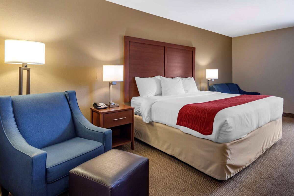 A hotel room with a large bed, a blue armchair, a small table, and two bedside lamps.