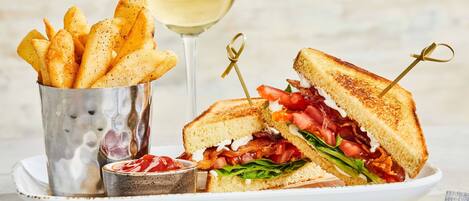 Ein halbiertes Sandwich, ein Glas Weißwein und eine Portion Pommes auf einem Teller.