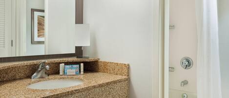 A bathroom with a granite countertop sink, a mirror, a framed picture on the wall, and a shower curtain.
