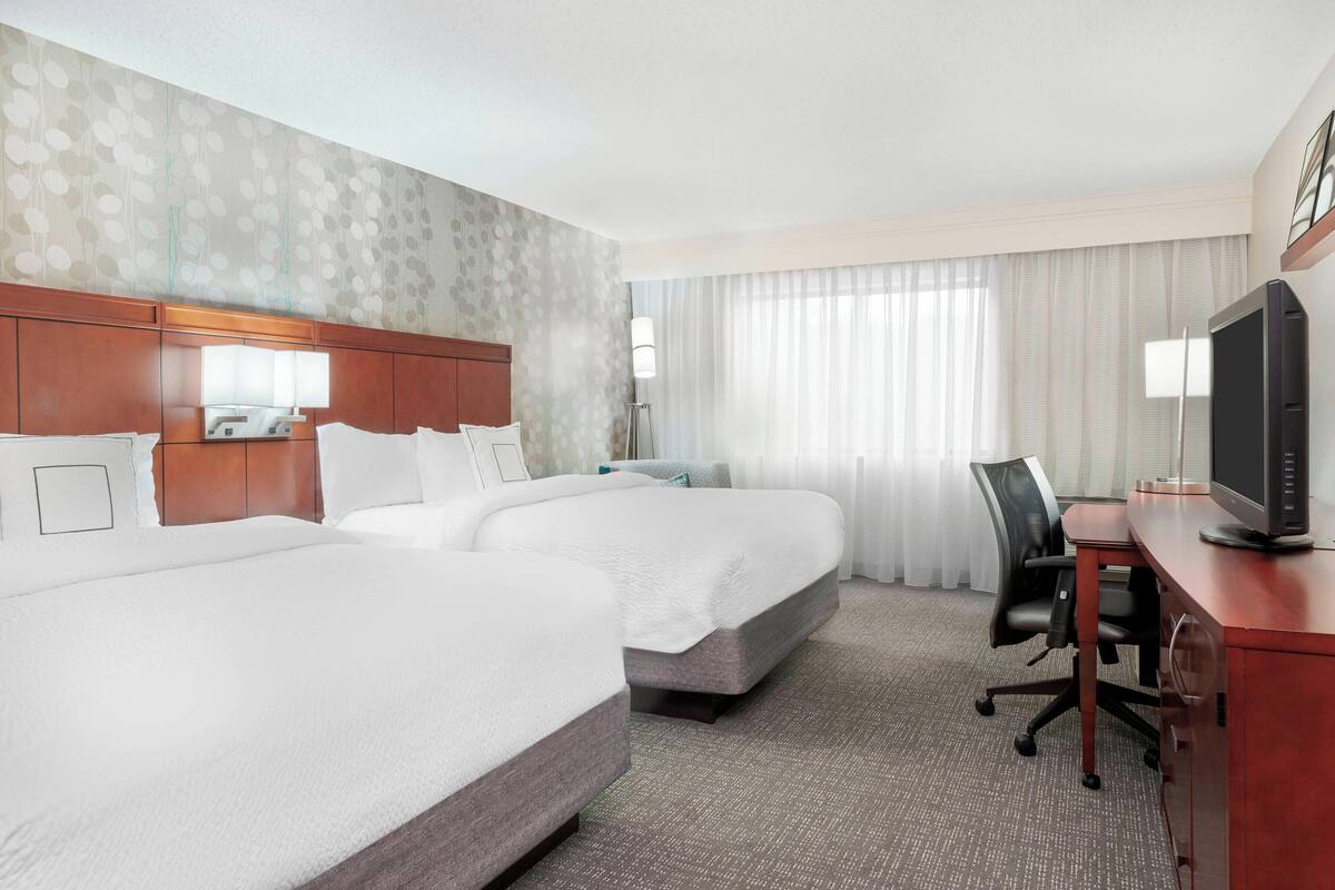 Ein Hotelzimmer mit zwei Betten, einem Schreibtisch mit Fernseher und einem Sessel.