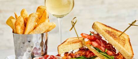 A plate with a grilled sandwich, a glass of white wine, and a container of fries.