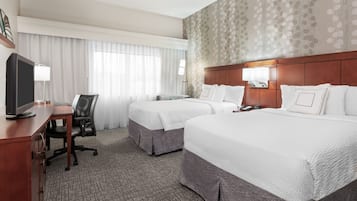 Una habitación de hotel con dos camas, un escritorio con computadora, una silla y un televisor.