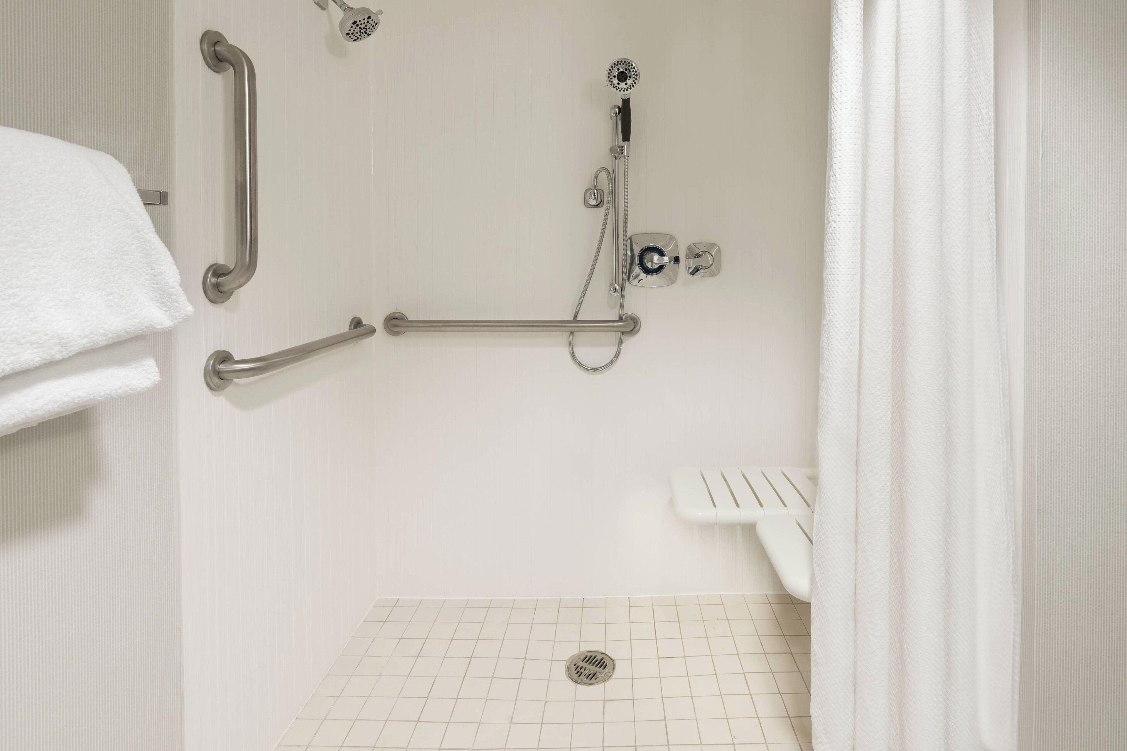 A bathroom with a walk-in shower, grab bars, a white toilet, and a white towel on the wall.