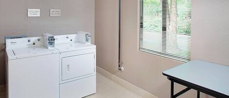 A laundry room with a washer and dryer, a table, and a window with blinds.