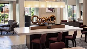 A modern hotel lobby with a central bar area, seating arrangements, and large windows offering views of the outdoors. - Courtyard Durham Near Duke University/Downtown (Durham)