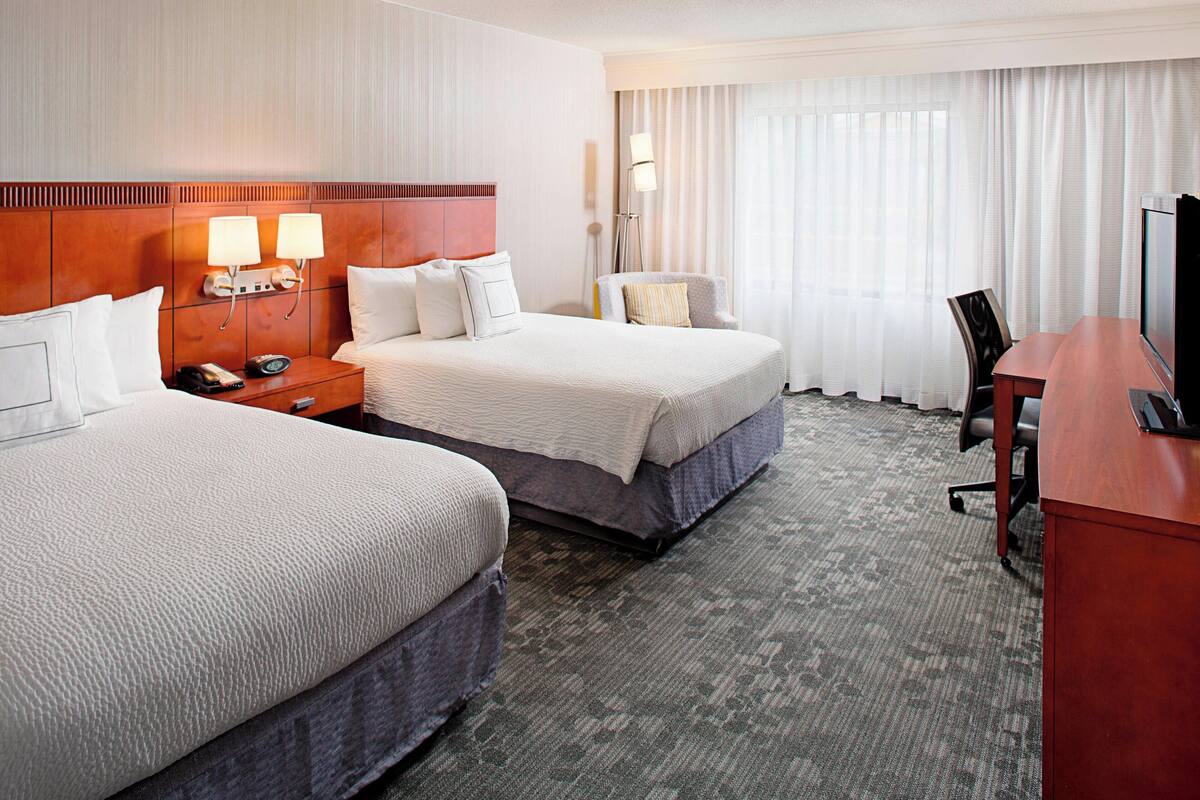 A hotel room with two beds, a desk, a chair, a TV, and a phone on the nightstand.