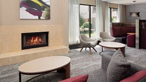 A modern living room with a fireplace, comfortable seating, and a large window offering a view of the outdoors. - Courtyard Durham Near Duke University/Downtown (Durham)