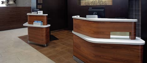 A reception area with a wooden reception desk and a smaller desk, both with white tops and metal bases.
