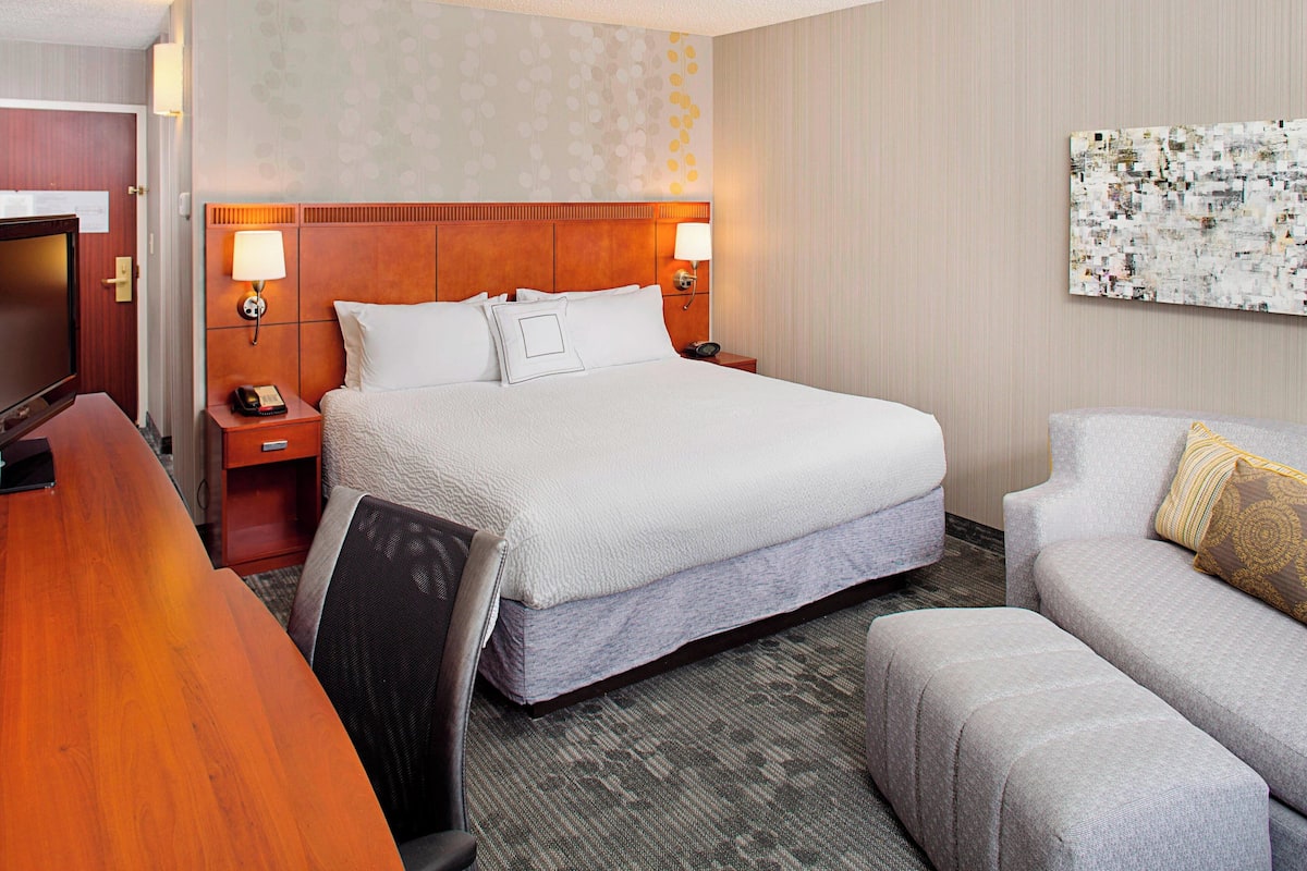 A hotel room with a large bed, a desk, a chair, a sofa, and a television.