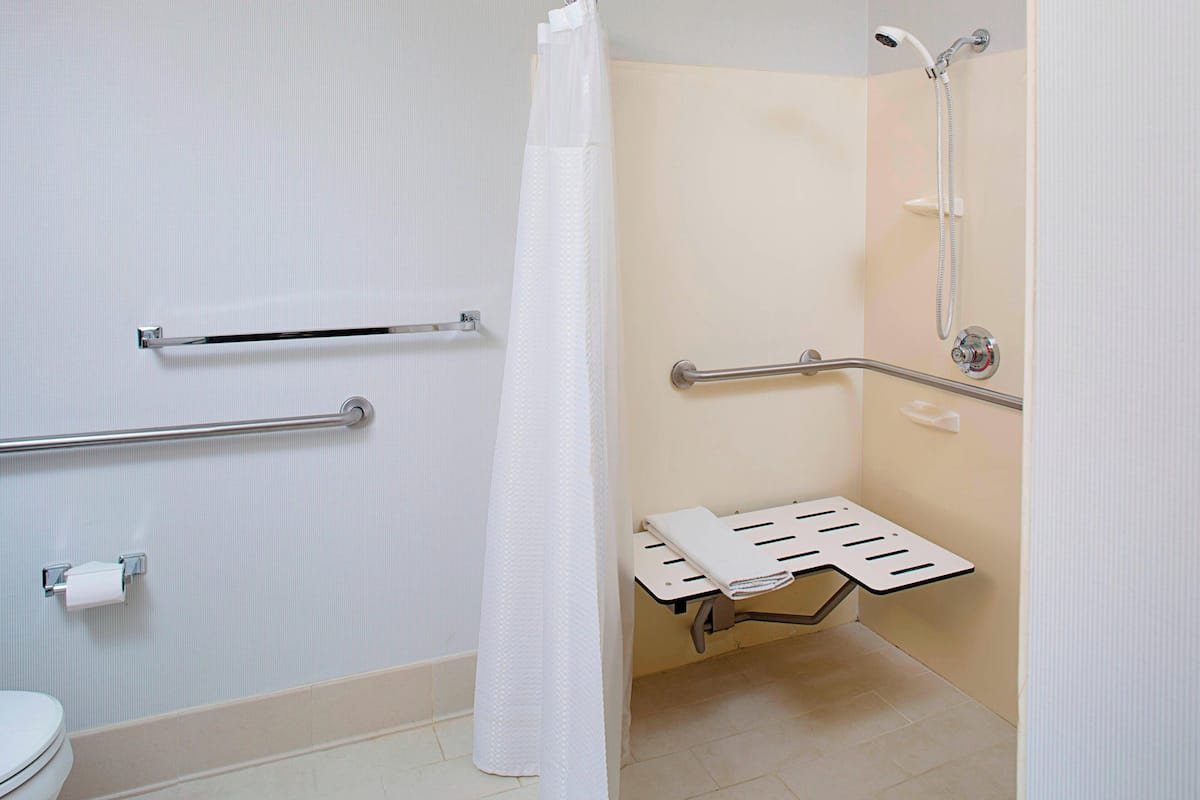 A bathroom with a shower, grab bars, a toilet, and a towel rack.