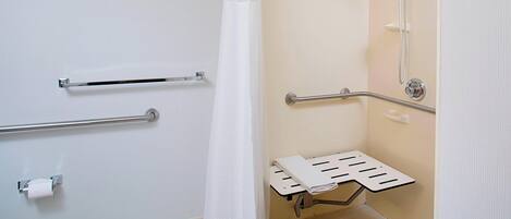 A bathroom with a shower, grab bars, a toilet, and a towel rack.