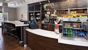 A modern bar area with a curved counter, bar stools, a coffee machine, and a refrigerated display of beverages. - Courtyard Durham Near Duke University/Downtown (Durham)