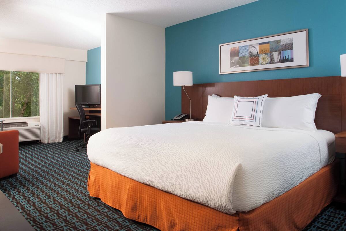 A hotel room with a large bed, a desk with a computer, a TV, and a window with curtains.