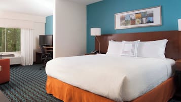 A hotel room with a large bed, a desk with a computer, a TV, and a window with curtains.