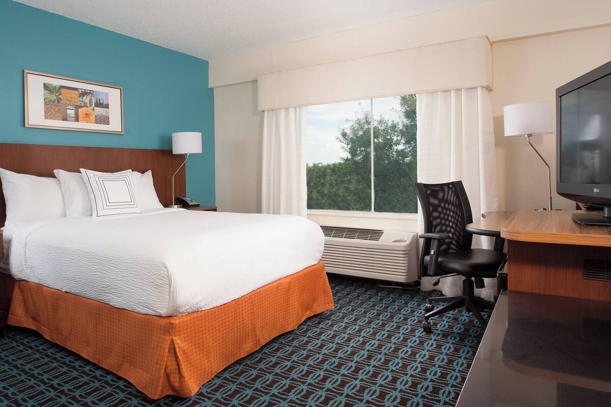 A hotel room with a bed, a desk, a chair, a television, and a window with curtains.