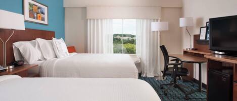 A hotel room with two beds, a desk with a television, and a large window with curtains.