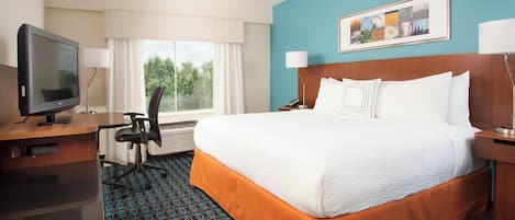 A hotel room with a large bed, a desk with a television, a chair, and a window with curtains.