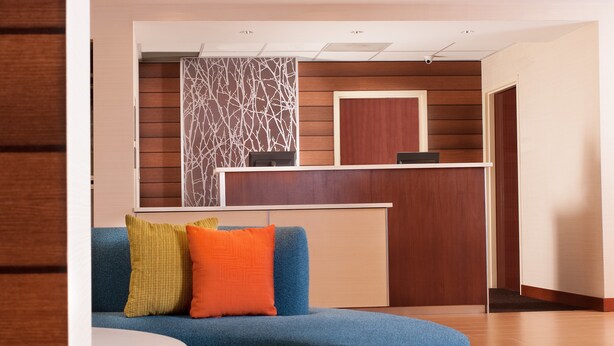 A reception area with a blue sofa, a small table, and a wooden reception desk. - Fairfield Inn by Marriott Charlotte Gastonia (Gastonia)