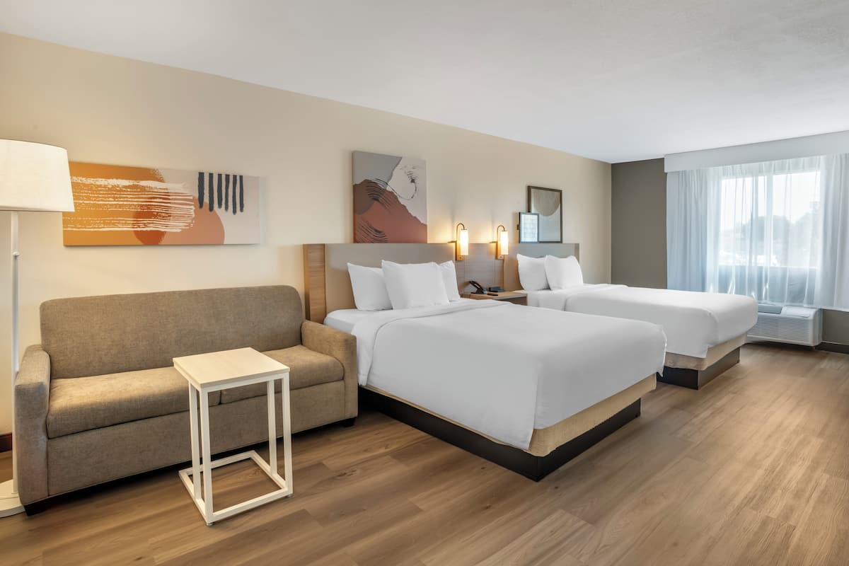 A hotel room with two beds, a sofa, a small table, and artwork on the walls.