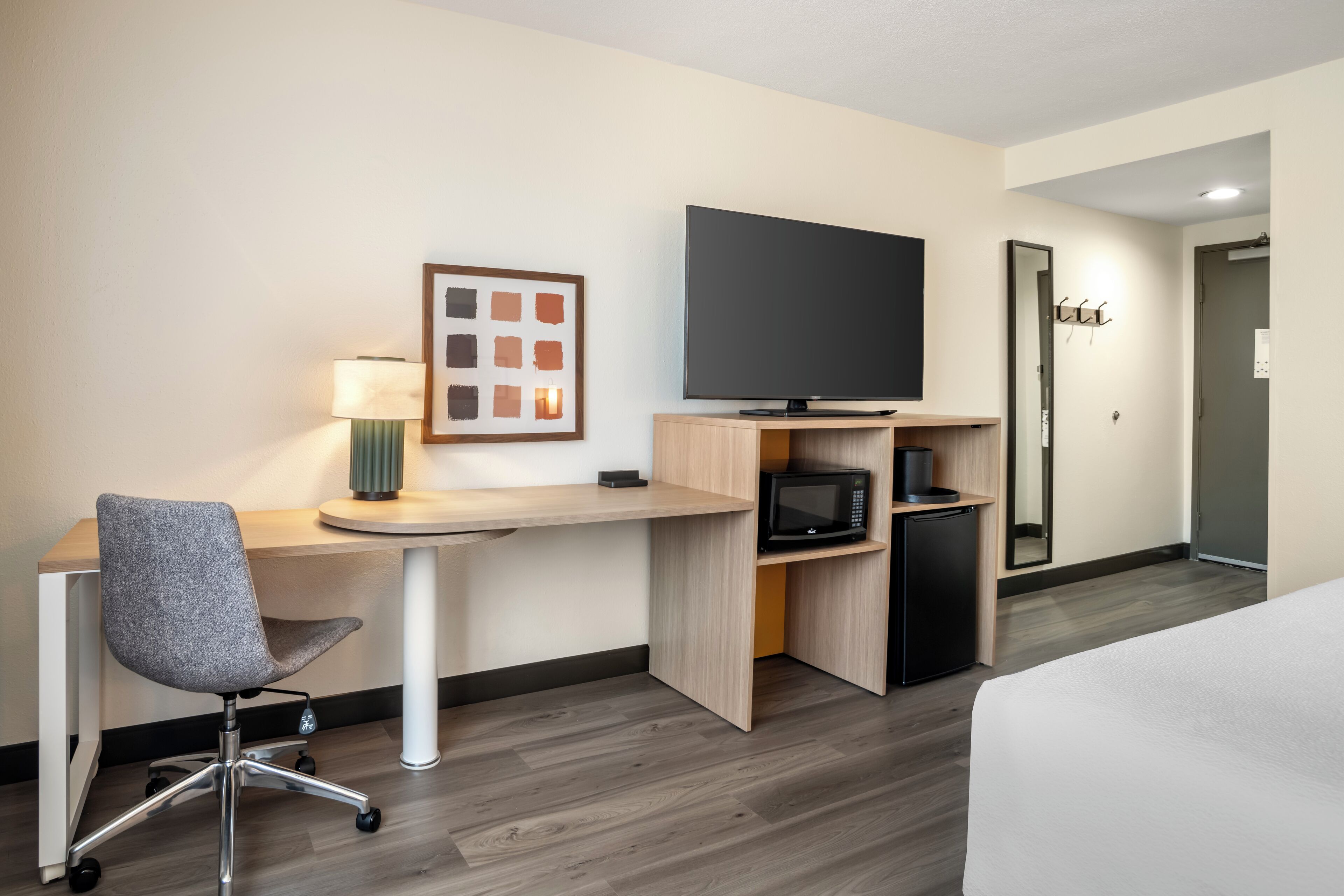 A hotel room with a desk, chair, television, microwave, and a bed.