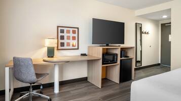 A hotel room with a desk, chair, television, microwave, and a bed.