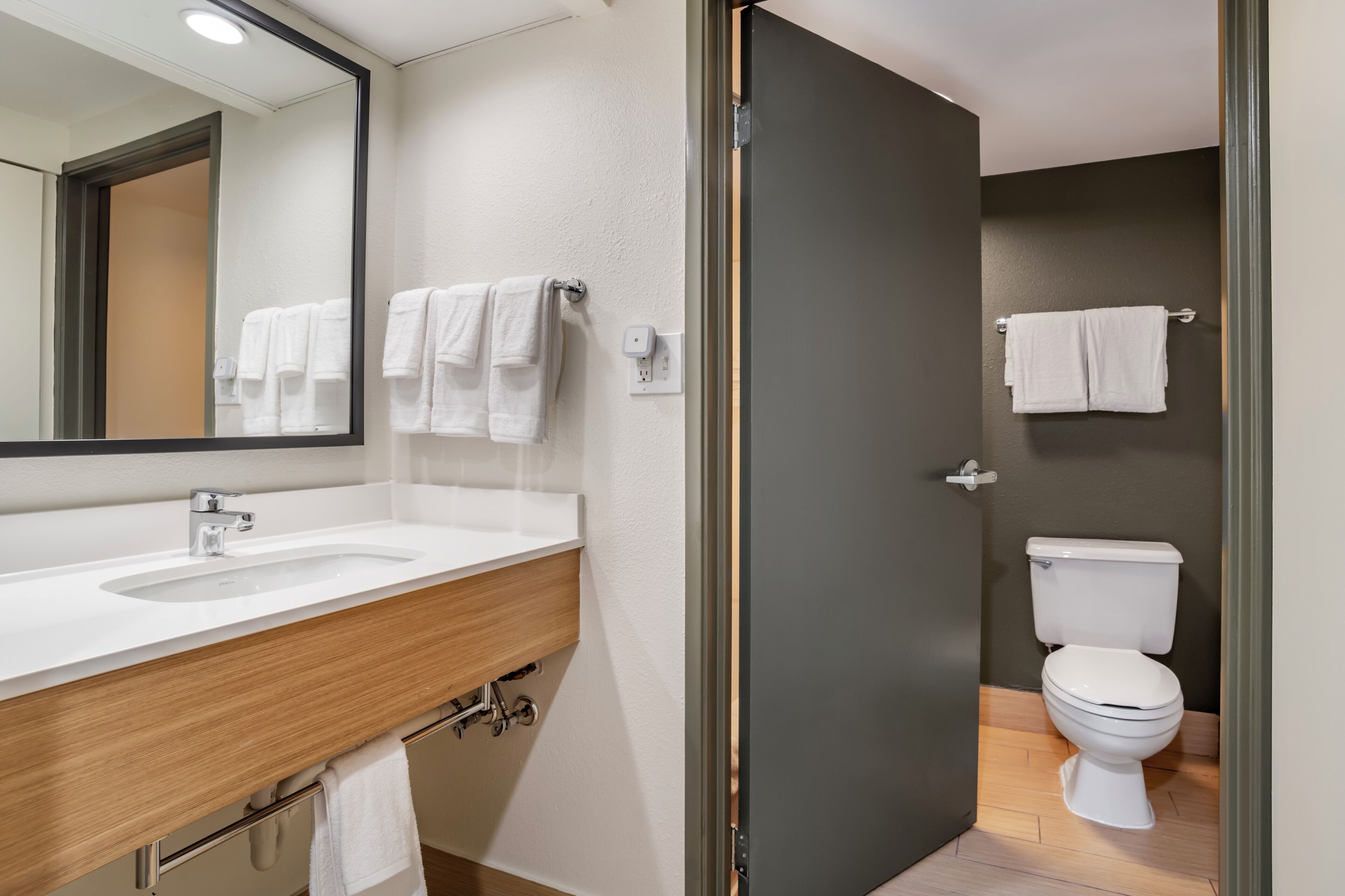 Un baño moderno con tocador de madera, lavamanos blanco, espejo y retrete.