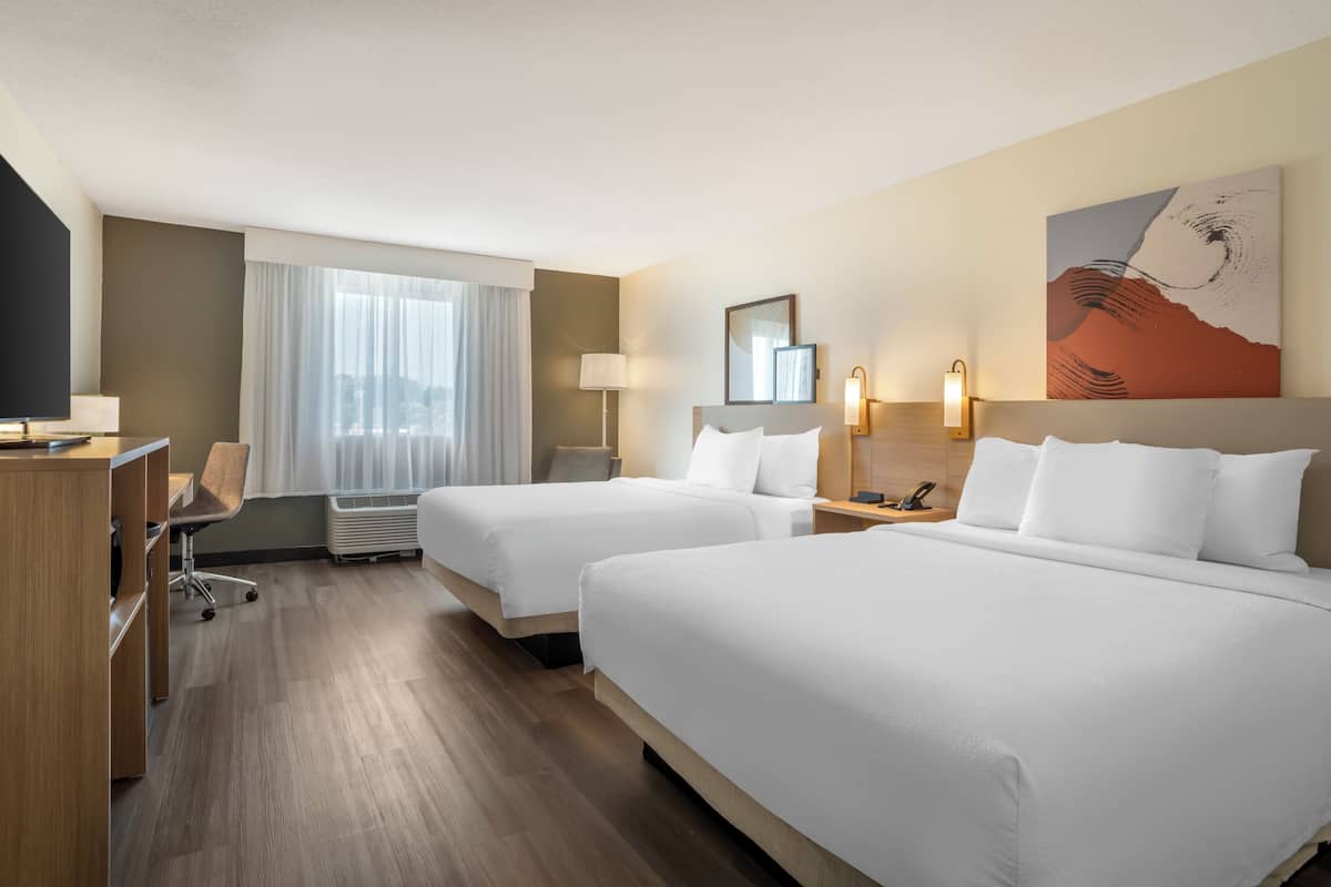 A hotel room with two beds, a desk, a chair, a TV, and a painting on the wall.