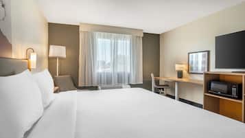 A hotel room with a large bed, a desk with a chair, a television, and a microwave.