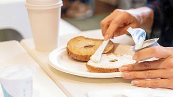 Eine Person verteilt Butter auf einer Brotscheibe auf einem Teller.