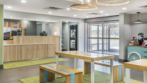 A modern reception area with a wooden reception desk, a refrigerator, and a seating area with tables and benches. - Spark by Hilton Kannapolis (Kannapolis)