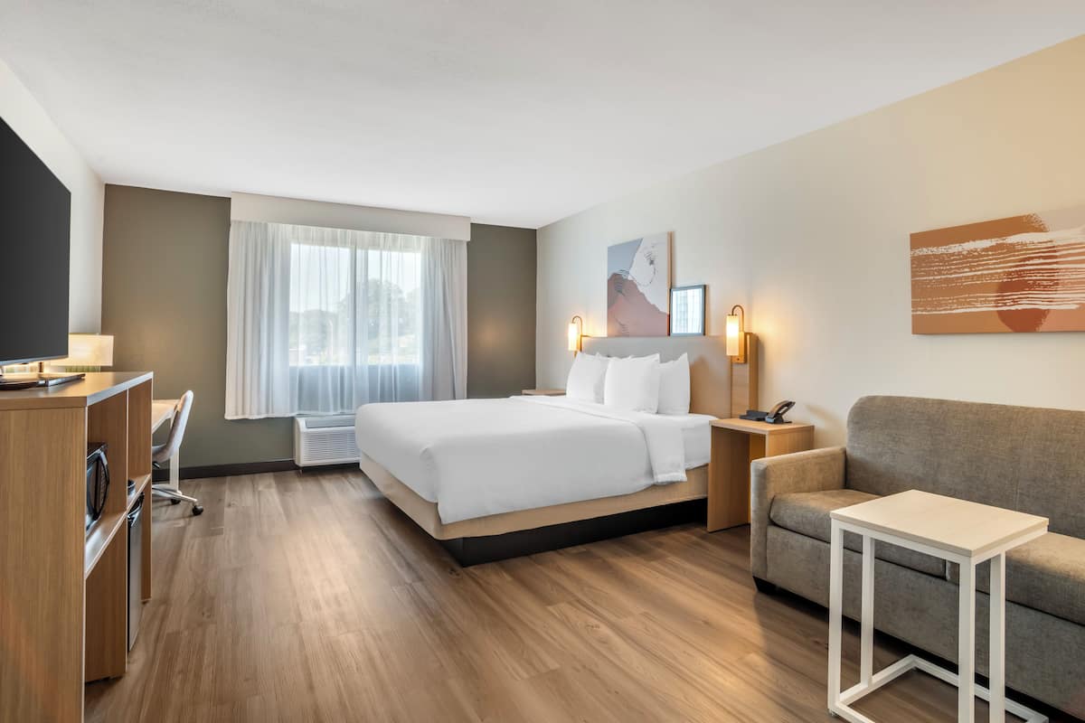 A modern hotel room with a bed, a sofa, a desk, and a small table.