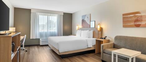 A modern hotel room with a bed, a sofa, a desk, and a small table.