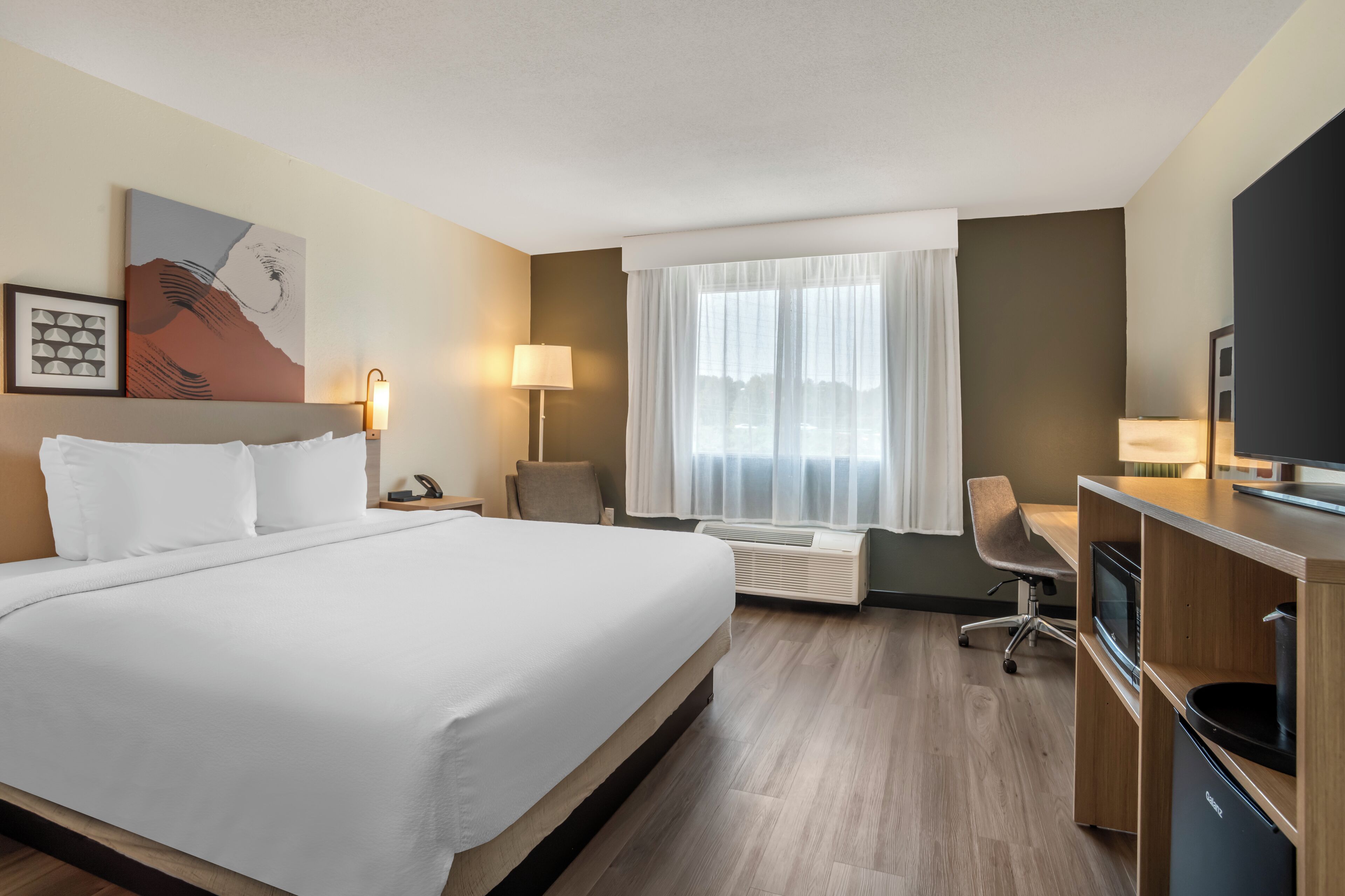 Een hotelkamer met een groot bed, een bureau met stoel, een televisie en een raam met gordijnen.