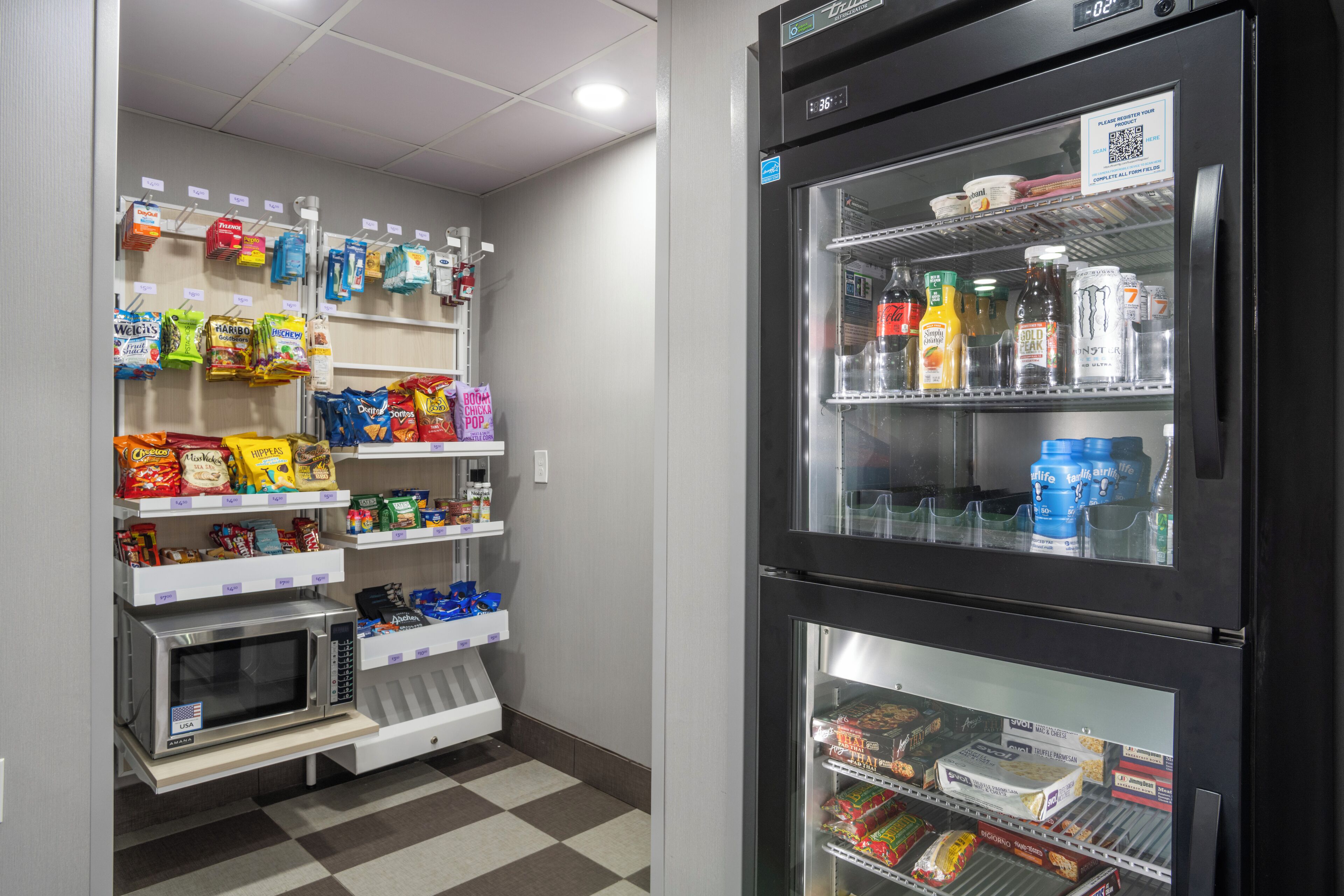 A self-service food area with microwaves, snack dispensers, and refrigerated shelves stocked with beverages and food items.