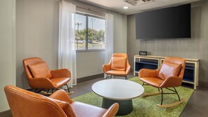 A hotel room with a large flat-screen TV, a round table, and four orange leather chairs. - Spark by Hilton Kannapolis (Kannapolis)