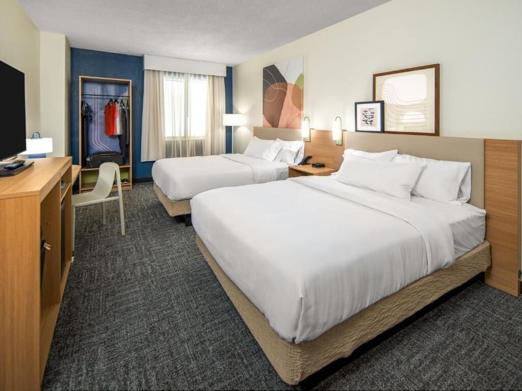 A hotel room with two beds, a desk, a chair, a wardrobe, and a TV.