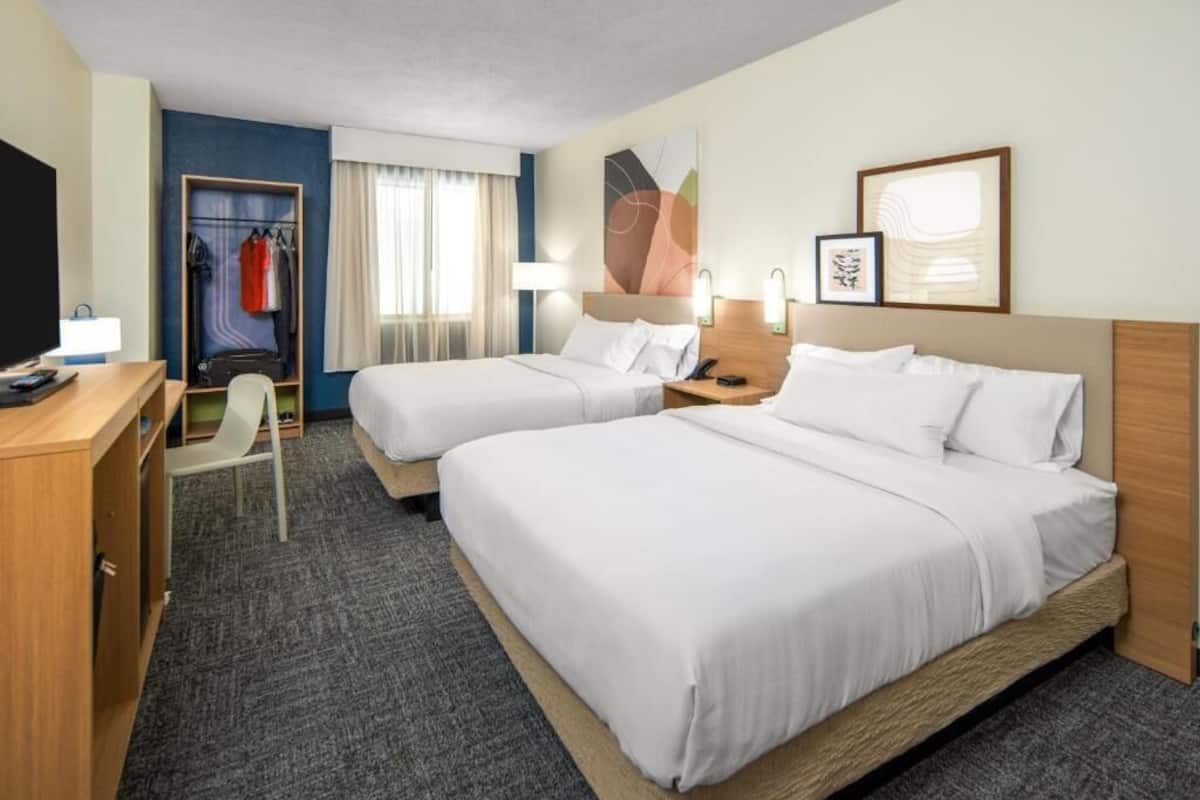 A hotel room with two beds, a desk, a chair, a wardrobe, and a TV.