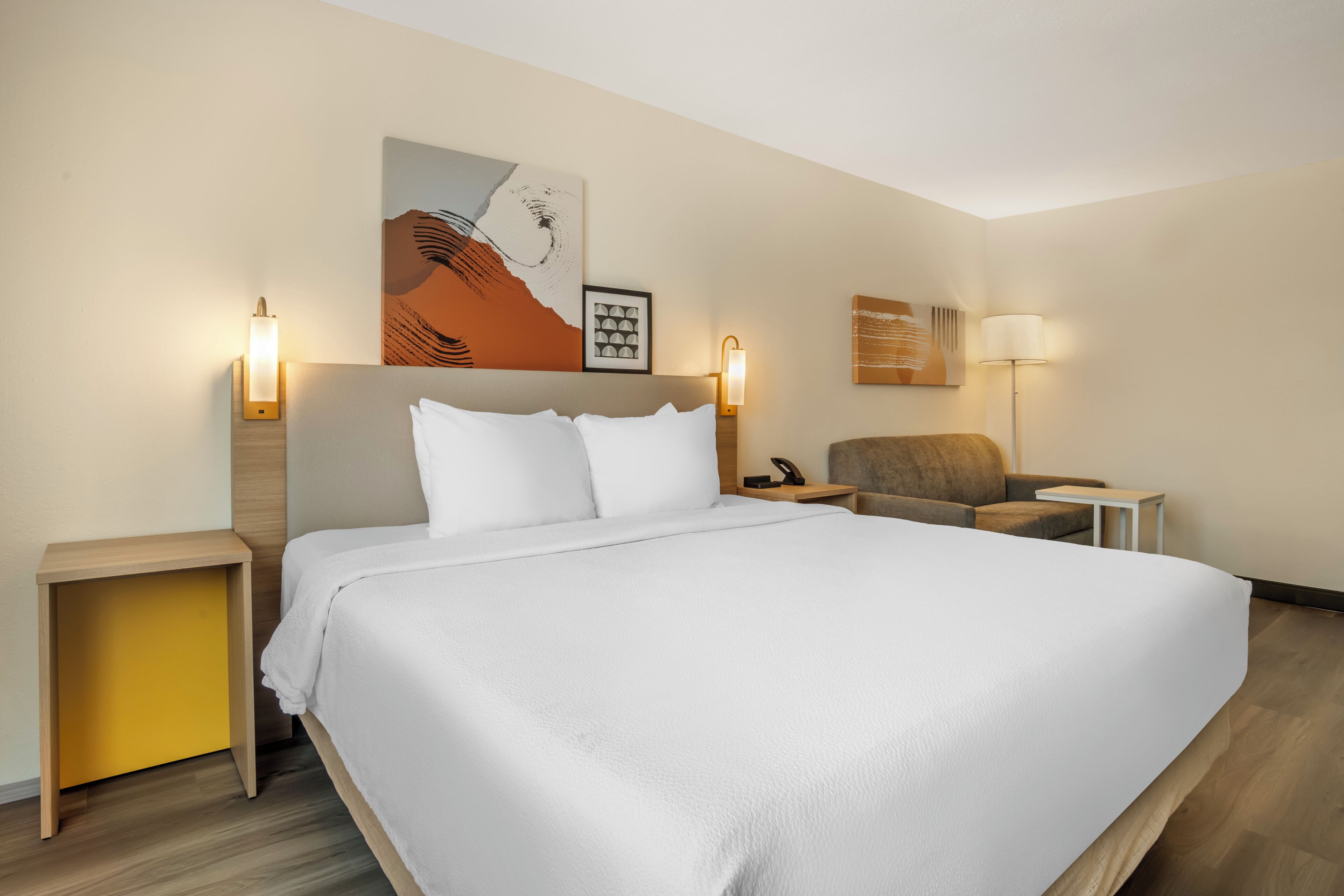 Een hotelkamer met een groot bed, een stoel, een bureau en kunstwerken aan de muur.