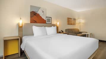 Een hotelkamer met een groot bed, een stoel, een bureau en kunstwerken aan de muur.
