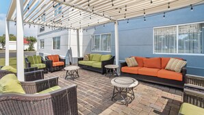 A covered outdoor seating area with wicker furniture and a blue wall. - Spark by Hilton Kannapolis (Kannapolis)