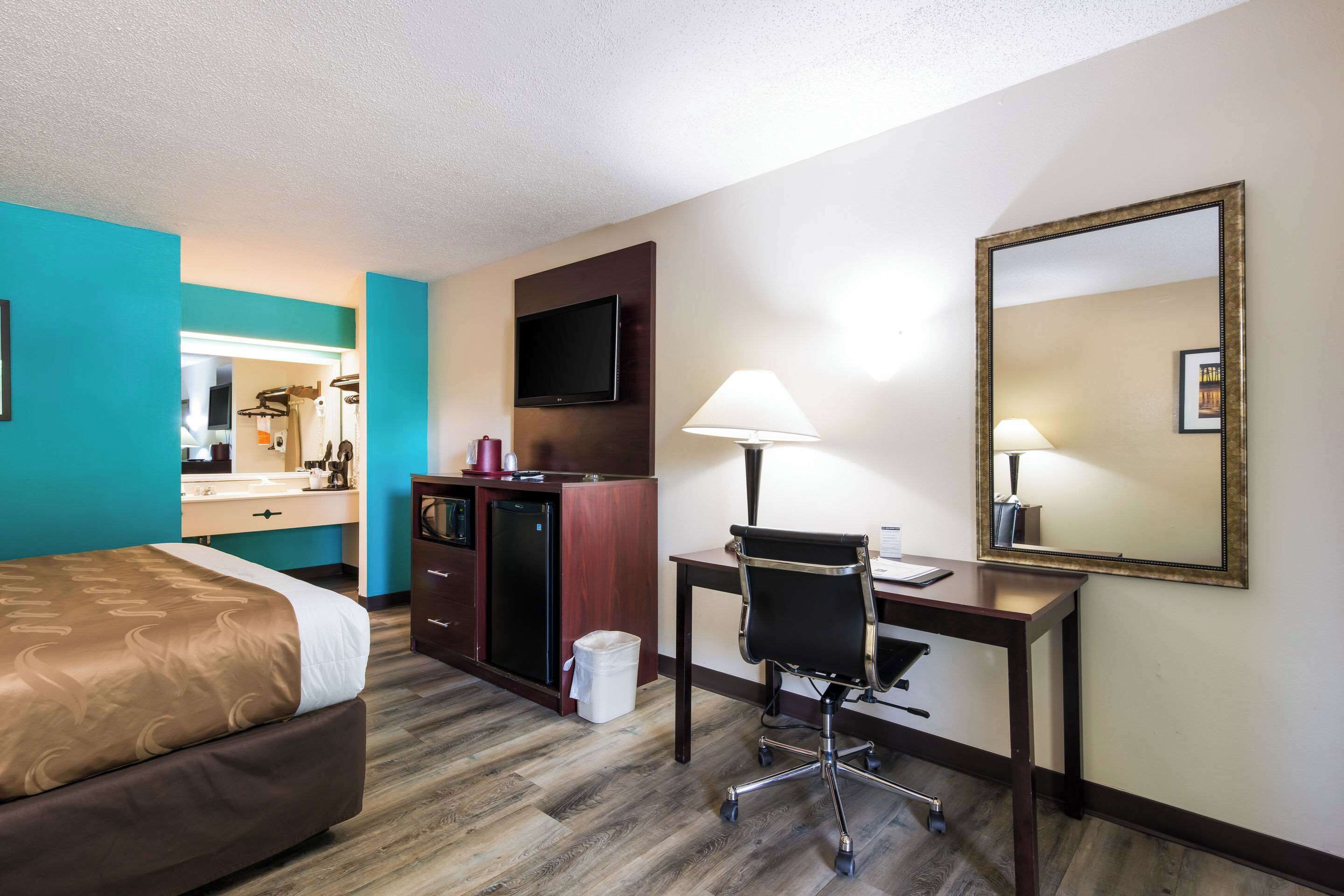 Een hotelkamer met een bed, bureau, stoel, televisie en een spiegel.