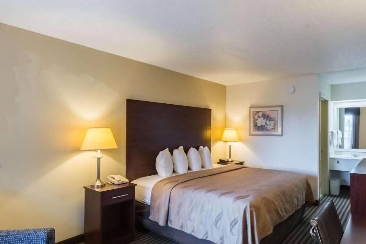 Ein Hotelzimmer mit Bett, Nachttischlampen, Schreibtisch und Spiegel.