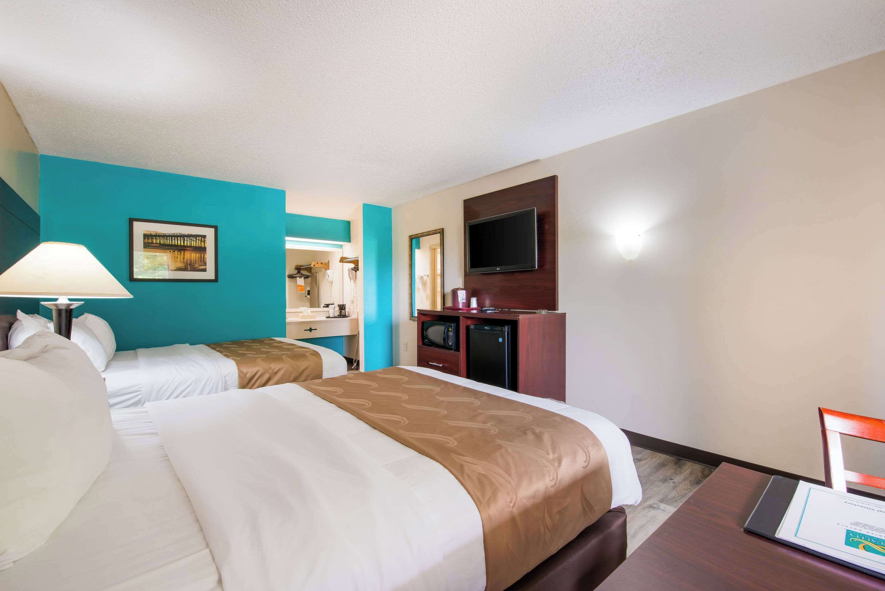 A hotel room with two beds, a desk, a TV, and a mirror.