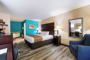 A hotel room with a bed, bedside tables, a desk, a chair, a mirror, and a blue accent wall.